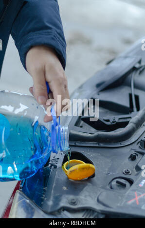Voce maschile è in possesso di una bottiglia di antigelo blu in mani e versando il liquido antigelo per il lavaggio di auto schermo. Foto Stock