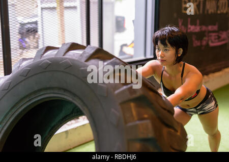 Asia donna fitness di spinta e di ribaltamento ruota carrello pneumatico in palestra Foto Stock