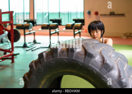 Asia donna fitness di spinta e di ribaltamento ruota carrello pneumatico in palestra Foto Stock