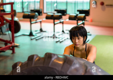 Asia donna fitness di spinta e di ribaltamento ruota carrello pneumatico in palestra Foto Stock