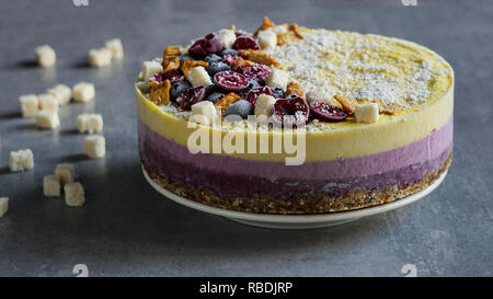 Materie vegane berry e mango cheesecake senza glutine su un bianco sullo sfondo di legno di noce di cocco Foto Stock