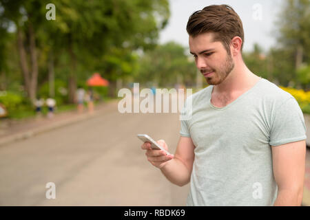 Ritratto di giovane uomo bello utilizzando il telefono cellulare in posizione di parcheggio Foto Stock