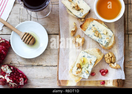 Panini con formaggio blu, melograno, miele e noci servita con vino rosso. Stile rustico. Foto Stock