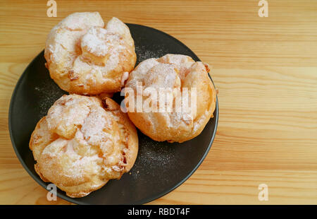 Vista superiore di tre Choux a la Creme Dolci o Francese Bignè su una piastra nera servita su un tavolo di legno Foto Stock