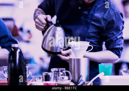 Professional barista versando acqua bollente dal bollitore speciale nel filtro, per la preparazione di caffè filtro. Viola colore di sfondo Foto Stock