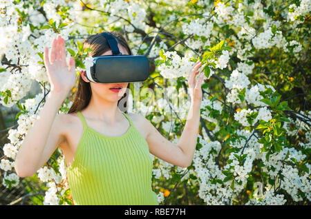 Esperienza di VR. Signora giovane indossare occhiali vr in primavera la natura. Pretty girl in realtà virtuale auricolare. Ragazza carina giocare in giardino di primavera. Innovativa tecnologia di VR. La tecnologia virtuale di simulazione Foto Stock