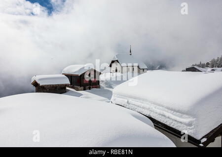 Coperta di neve rifugi di montagna e chiesa circondato da nuvole di Bettmeralp distretto di Raron nel canton Vallese Svizzera Europa Foto Stock