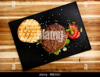 Vista in pianta di un succulento e succosa rare hamburger di manzo con pomodoro e guarnire crescione, in una focaccia di pane, su una piastra di ardesia Foto Stock