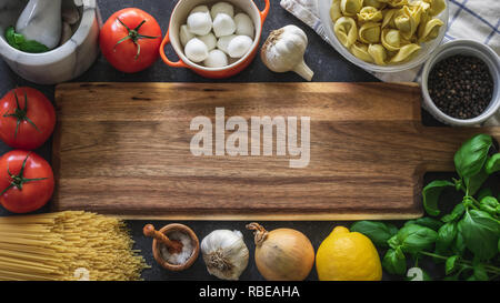 Il cibo italiano di cottura Ingredienti. Tagliere circondato da verdure, mozzarella, erbe e pasta. Vista da sopra con copia spazio. Foto Stock