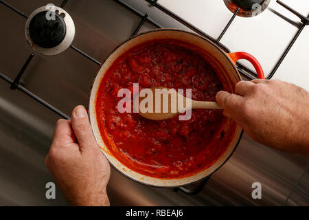 Vista in pianta di una pentola di gormet tradizionale salsa di pomodoro e il cucchiaio di legno su un acciaio inossidabile piano cottura Foto Stock