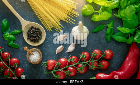 Il cibo italiano di cottura Ingredienti. Pomodori, spaghetti, basilico, aglio e spezie di stagionatura in pietra scura sullo sfondo. Foto Stock