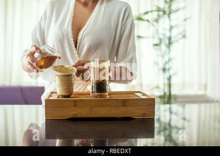 Godendo della cerimonia del tè. Vista laterale Ritratto di giovane donna bella in kimono holding tazza di tè cercando di copiare lo spazio mentre in piedi contro uno sfondo bianco con albero verde. Libera posto vuoto per il testo Foto Stock