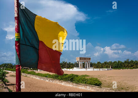 Il flag Beninese in primo piano con la porta di non ritorno (Porte du non retour) a Ouidah in background, un ex schiavi post in Benin. Foto Stock