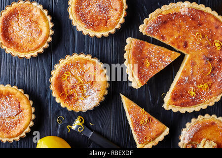 Pasqua svizzera dessert - crostate di semola spolverati con zucchero a velo e la scorza di limone, gateau de Paques, Osterfladen, su una tavola nera con limone, horizo Foto Stock