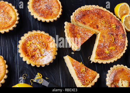 Pasqua svizzera dessert - crostate di semola spolverati con zucchero a velo e la scorza di limone, gateau de Paques, Osterfladen, su una tavola nera con limone, horizo Foto Stock