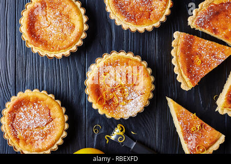 Pasqua svizzera dessert - torte di riso spolverati con zucchero a velo e la scorza di limone tagliata a fettine, gateau de Paques, Osterfladen, su una tavola nera con lem Foto Stock