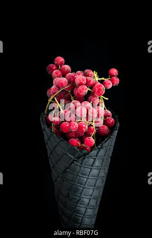 Nero cono di wafer con il ribes rosso congelato frutti. Un sano gelato. Foto Stock