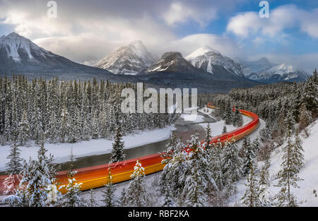 Treno in movimento attraverso la montagnosa curvo Canadian Rockies con moto sfocata in giornata invernale con coperta di neve alberi e montagne Foto Stock