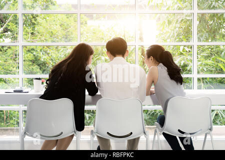 Un gruppo di tre giovani asiatici business persone riunite insieme a un tavolo per discutere un'idea interessante nella caffetteria. Foto Stock