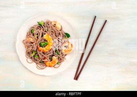 Una foto aerea di soba, Tagliatelle di grano saraceno con gamberi e verdure, ripresa dall'alto con bacchette su un pallido sfondo di legno Foto Stock