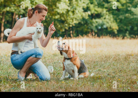 Vista ravvicinata di attraenti montare donna inginocchiata vicino al suo cane, formazione di lui. Giovane ragazza con gatto bianco dando i comandi e le richieste al suo cane, per esterno Foto Stock