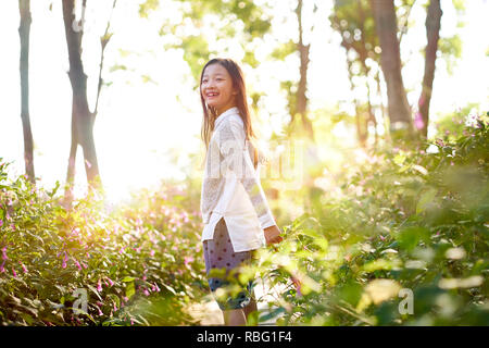 8 anno-vecchio bella ragazza asiatica in piedi nel campo dei fiori guardando indietro e sorridente. Foto Stock