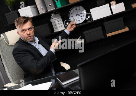 Imprenditore seduti al tavolo per computer e punti le sue mani a fronte di clock Foto Stock