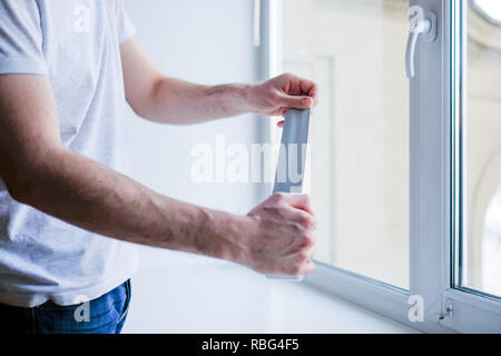 Lavoratore di mettere il nastro di tenuta sulla finestra in casa Foto Stock