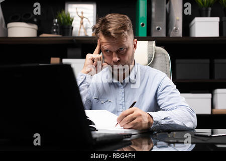 Giovane uomo seduto al tavolo per computer e rende note nel diario Foto Stock