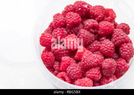 Lamponi maturi in un secchio di plastica su uno sfondo luminoso Foto Stock