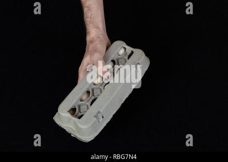 Maschio lato tenendo un cartone uovo scatola piena di uova di gallina in feltro nero lo sfondo. Foto Stock