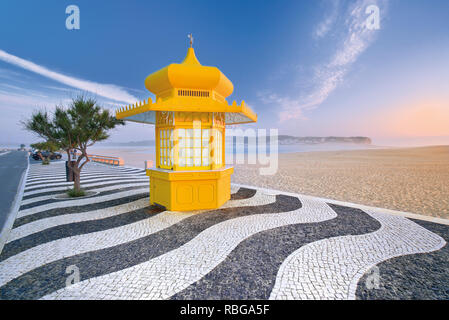 Chiosco giallo su ciottoli marciapiede in pietra con in bianco e nero ornamento ad ampio solitaria spiaggia di sabbia Foto Stock