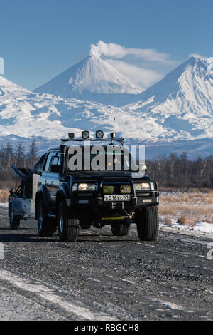 SUV giapponese Toyota Land Cruiser con rimorchio che trasporta motoslitta, sled guidare sulla strada contro il fondale di Kluchevskaya gruppo di vulcani Foto Stock