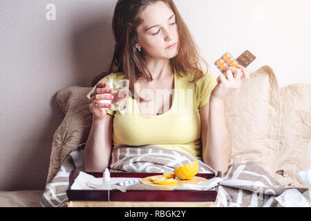 Una ragazza con un mal di testa e influenza a letto è trattata con compresse e vitamine. Raffreddori stagionali in inverno Foto Stock