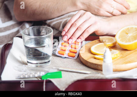 Pillole di termometro acqua e limone sul vassoio. Una persona con un freddo viene trattato in letto. Raffreddori, influenza e trattamento Foto Stock