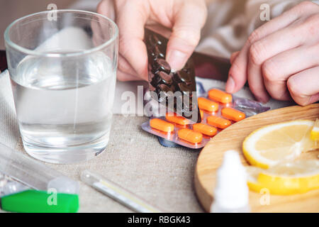 Pillole di termometro acqua e limone sul vassoio. Una persona con un freddo viene trattato in letto. Raffreddori, influenza e trattamento Foto Stock