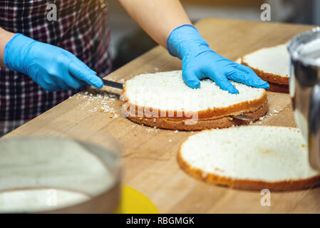Pastry chef in guanti taglia il biscotto in strati di fare la torta. Concetto di produzione di prodotti a base di zuccheri Foto Stock