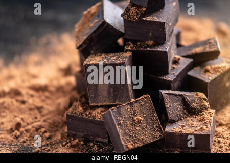 Pezzi di dark cioccolato amaro con cacao in polvere di legno scuro dello sfondo. Il concetto di ingredienti dolciari Foto Stock