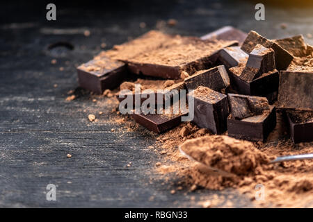 Pezzi di dark cioccolato amaro con cacao in polvere di legno scuro dello sfondo. Il concetto di ingredienti dolciari Foto Stock