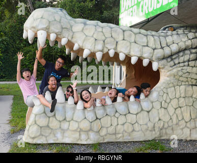 Un gruppo di turisti cinesi in posa la bocca aperta di una statua del coccodrillo in un fiume Daintree crociere prenotazione chiosco, Parco Nazionale Daintree, lungi Nort Foto Stock