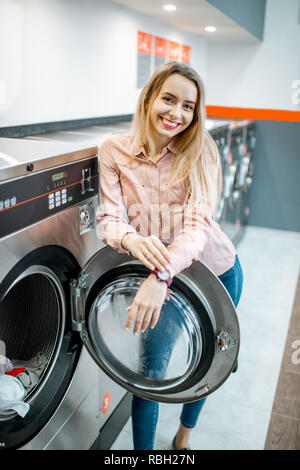 Ritratto di una giovane donna sorridente in piedi nel self-service lavanderia pubblica Foto Stock