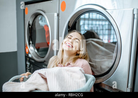 Giovani e allegra donna godendo il procedimento di lavaggio in piedi vicino a professional macchina asciugatrice di biancheria Foto Stock