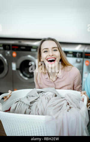 Ritratto di una donna allegra in piedi con ceste piene di panni da lavare in lavanderia self-service Foto Stock