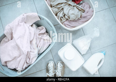 Panni sporchi in cesti con detergenti sul pavimento, vista da sopra Foto Stock