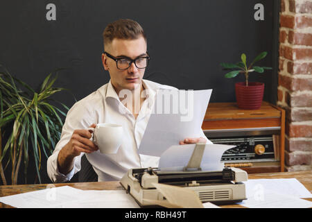 Un giovane scrittore che indossano occhiali camicia bianca e la lettura di un nuovo capitolo del suo libro e di bere il caffè della mattina Foto Stock