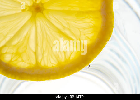 Fettina di limone retroilluminato in un bicchiere di acqua vista da vicino Foto Stock