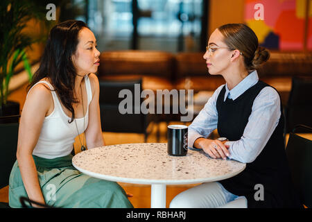 Due giovani donne hanno un incontro insieme in un ufficio durante il giorno. Essi sono da un team diversificato, uno è caucasico altri cinesi. Foto Stock
