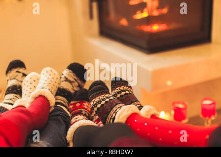 La grande famiglia è in fase di preriscaldamento vicino al caminetto in inverno freddo giorno. Interiour moderno, concentrarsi sulle calze Foto Stock