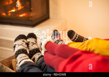 La grande famiglia è in fase di preriscaldamento vicino al caminetto in inverno freddo giorno. Interiour moderno, concentrarsi sulle calze Foto Stock