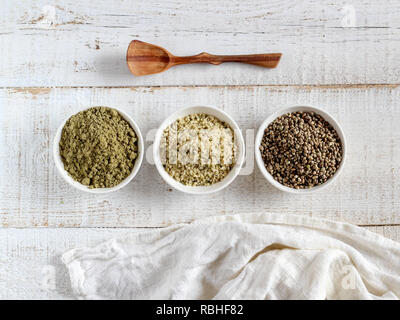 Organico tutta canapa semi, semi mondati e proteine in polvere in recipienti su un bianco sullo sfondo di legno Foto Stock